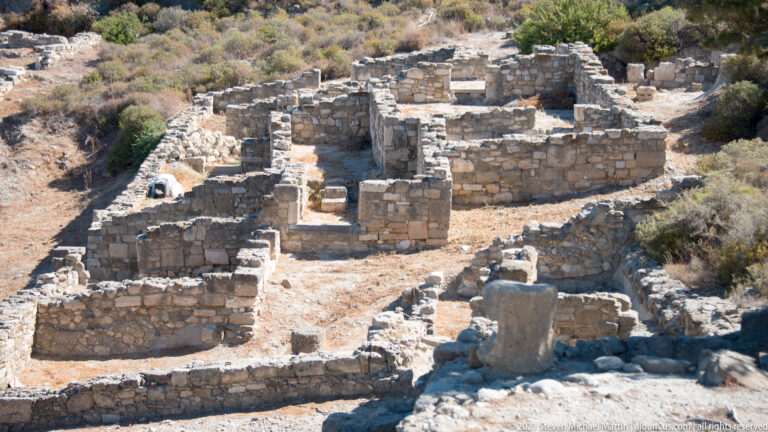 Elevated view of connected rectangular stone rooms, openings, and a central passage in the Ancient Kamiros residential ruins.