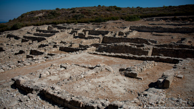 Broad elevated view of low stone walls forming many adjoining rooms and house plots in the Ancient Kamiros residential area.