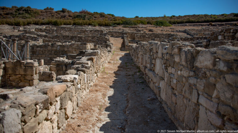 Narrow excavated passage with an earthen floor running between parallel stone walls at Ancient Kamiros.
