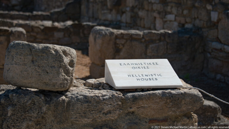 Stone site marker reading “Hellenistic House” placed on a wall among residential ruins at Ancient Kamiros.