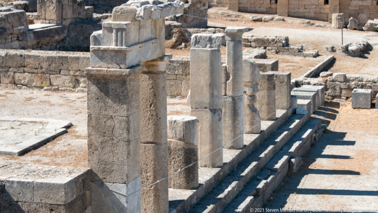 Close view of aligned stone piers and column shafts beside steps in a colonnaded area of Ancient Kamiros.