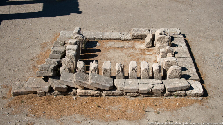 Small rectangular stone enclosure with a row of upright narrow elements set inside, viewed from above at Ancient Kamiros.