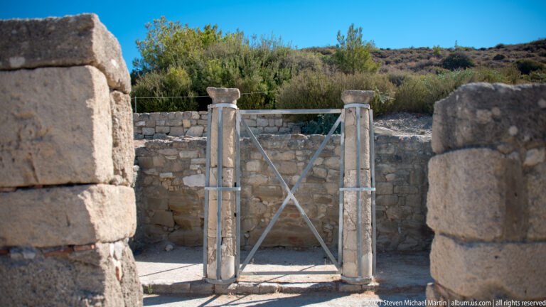 Two slender ancient columns reinforced by cross-braced metal supports between thicker stone walls at Ancient Kamiros.