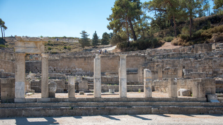 Partially reconstructed row of stone columns on a stepped platform before an ancient retaining wall.