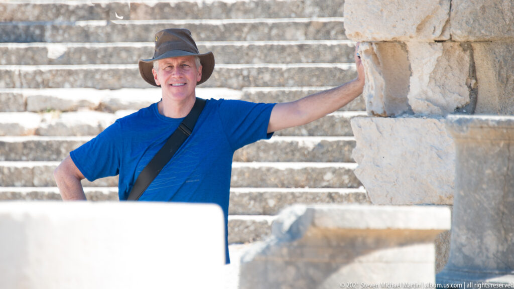 Visitor in a blue shirt and hat standing beside a large stone pier with ancient steps behind.