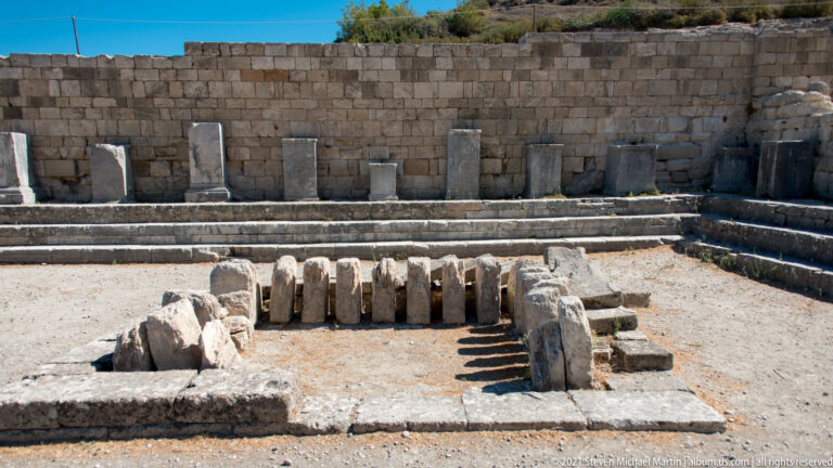Grouped stone architectural fragments in the foreground with pedestals and an ashlar wall behind.