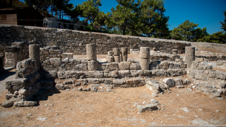 Circular masonry feature with several short cylindrical stone supports amid surrounding excavated walls.