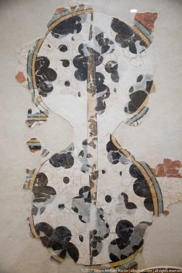 Fragmentary Mycenaean fresco pieces arranged on a pale backing with black, red, and curved colored motifs.