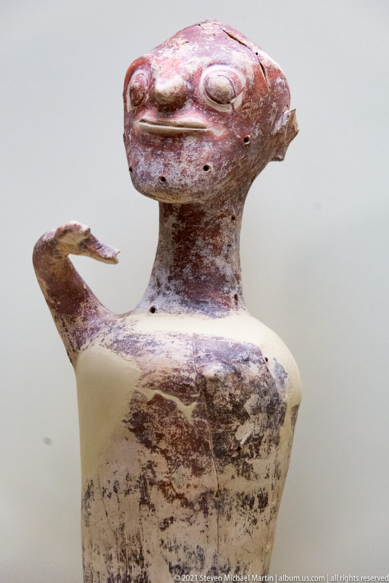 Stylized Mycenaean human-shaped ceramic vessel with broad head, projecting eyes, and outstretched arms.