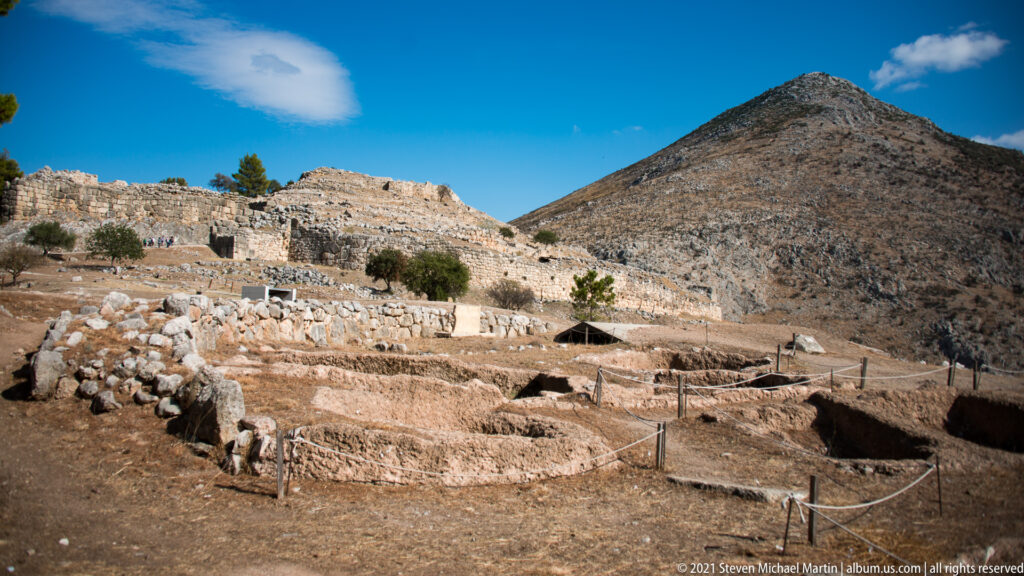 Excavated stone foundations and terraces at Ancient Mycenae with a steep mountain behind them.