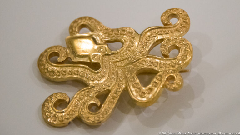 Close view of a small gold openwork ornament with curling loops and repeated raised circular decoration.