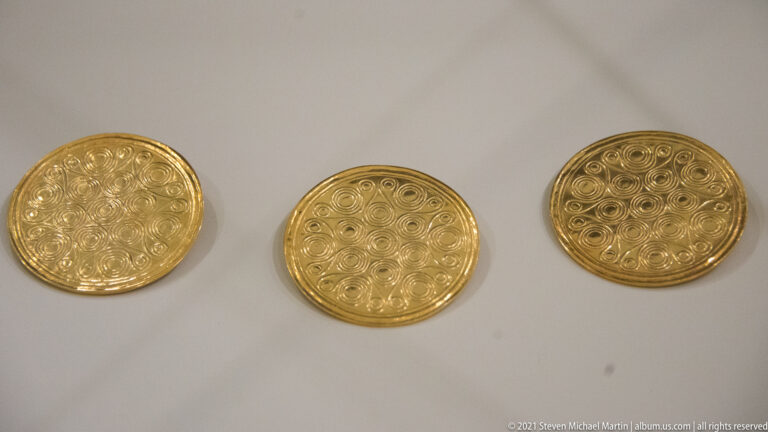 Three circular gold discs decorated with dense spiral patterns displayed side by side.