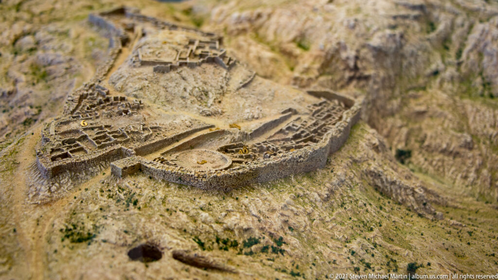 Oblique view of a scale model showing Mycenae's fortified citadel, walls, buildings, and sloping terrain.