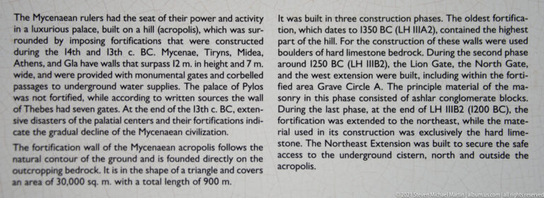 Interpretive panel with dense text describing the construction phases and layout of Mycenae's fortification walls.