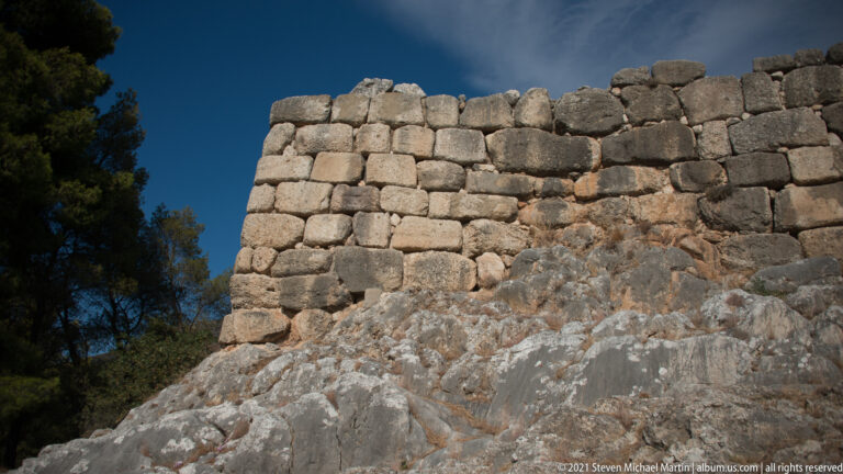 High Cyclopean wall of large stone blocks rising above a steep exposed bedrock outcrop.