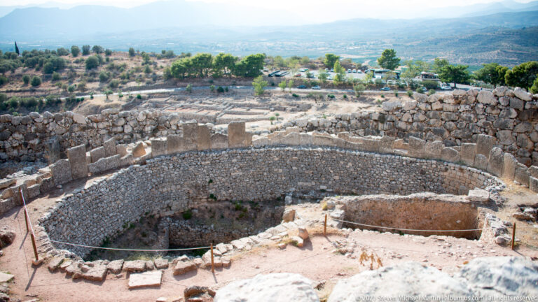 Elevated view of Grave Circle A, a large circular stone enclosure with interior burial areas and surrounding ruins.