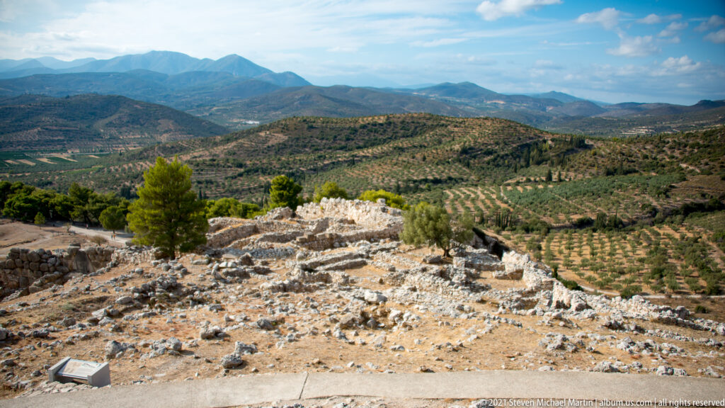 View from the citadel of Mycenae across ruins, olive groves, cultivated Argolid plain, and distant mountains.