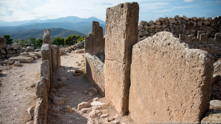 Upright dressed stone slabs standing among low foundations and rough masonry inside the citadel.