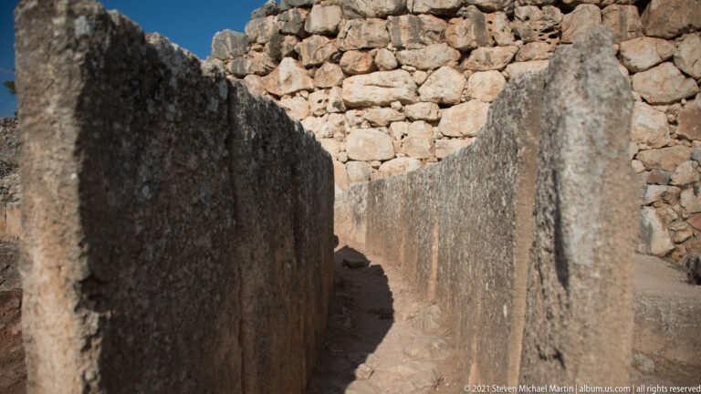 Narrow passage between tall dressed stone slabs with rough stone masonry behind.