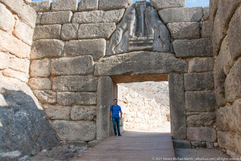 Visitor standing beneath a large stone gateway with massive lintel and triangular relieving feature above.