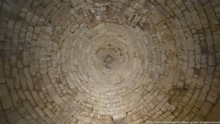 Upward view of concentric corbelled stone courses forming the domed interior of a Mycenaean tholos tomb.