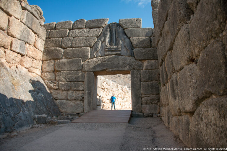 Paved approach to a massive stone doorway with a triangular relieving feature and visitor beyond.