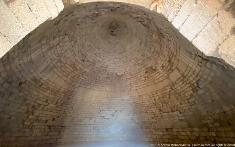 Oblique upward view inside a beehive tomb showing corbelled stone courses converging at the apex.