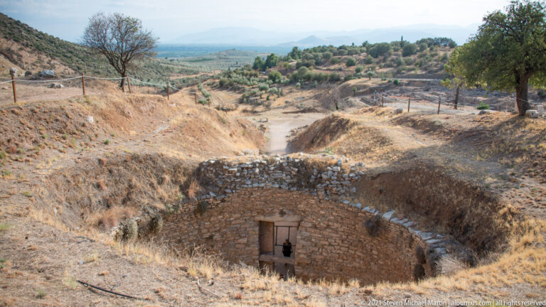 Sunken stone-lined approach descending to the rectangular doorway of a Mycenaean tholos tomb.