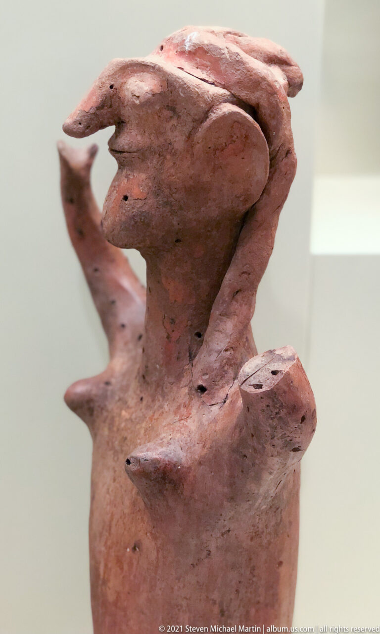 Fragmentary terracotta anthropomorphic figurine with prominent head, projecting arms, and worn hand-modeled surface.