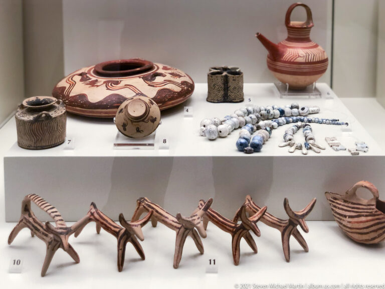Painted vessels, beads, small ornaments, and a row of four-legged terracotta figurines displayed together.