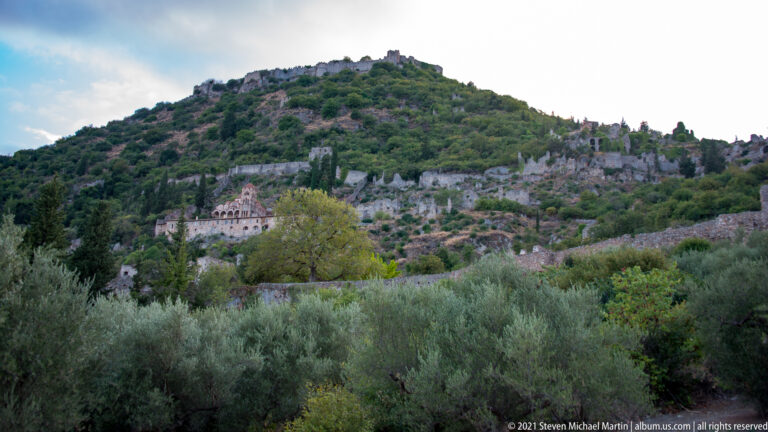 Wide view of Pantanassa Monastery amid trees, walls, and ruins on the steep Mystras hillside.