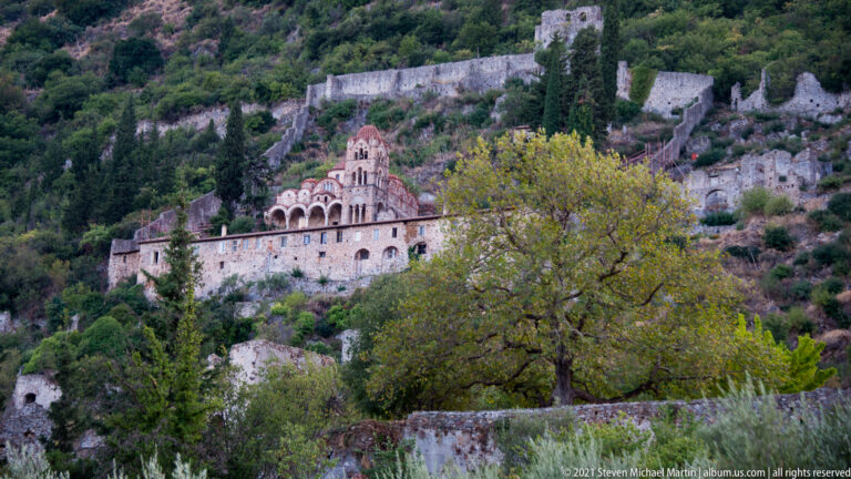 Domed Pantanassa Monastery church stands below a long defensive wall on the wooded Mystras slope.
