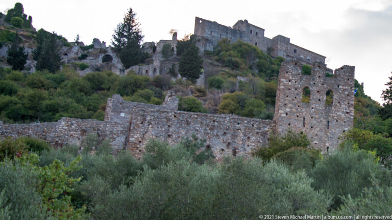 Stone towers and walls ascend the upper slope of Mystras toward ruins on the ridge.