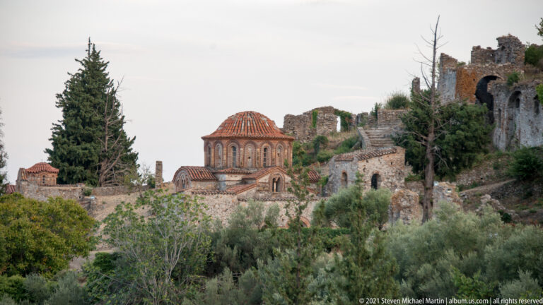 Hagia Sophia at Mystras with broad tiled dome, brick-framed windows, and surrounding stone ruins.