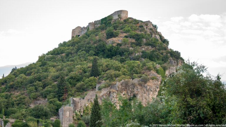Fortress walls crown the rocky summit of Mystras above a steep, densely vegetated hillside.