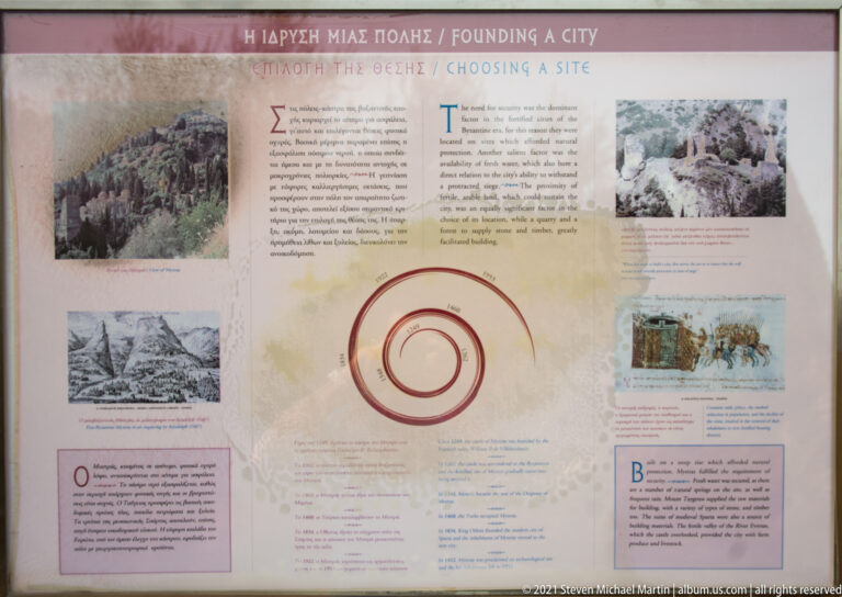 Bilingual interpretive panel at Mystras about founding the city and choosing the site, with maps, illustrations, and explanatory text.