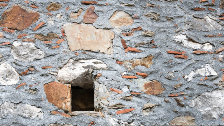 Close view of a rubble-stone wall at Mystras with brick fragments, mortar, and a small rectangular opening.