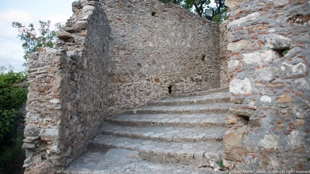 Narrow stone stairway climbing between thick ruined masonry walls at Mystras.
