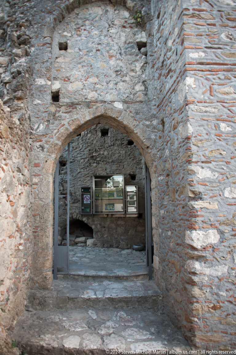 Pointed masonry arch at Mystras opening into a sheltered interior with display cases beyond.