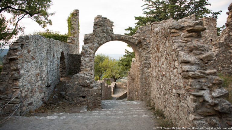 Brick-trimmed arch over a descending stone passage between ruined walls at Mystras.