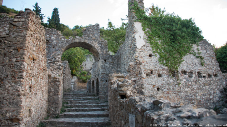 Stone steps rise through a semicircular arch between ivy-covered ruined walls at Mystras.
