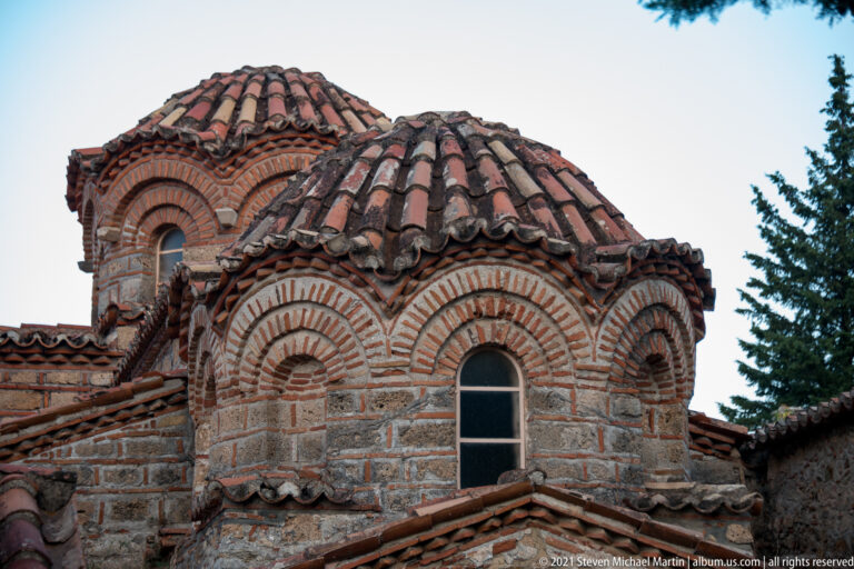 Close view of tiled Byzantine church domes at Mystras with concentric brick arches around narrow windows.