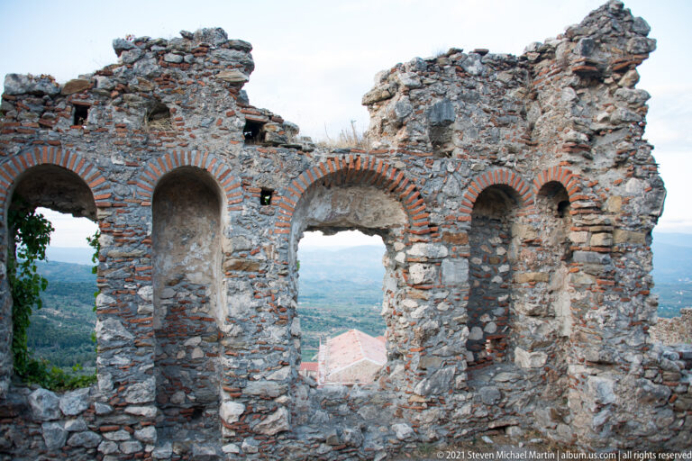Roofless ruined wall at Mystras with a row of brick-framed arches and niches overlooking the valley.
