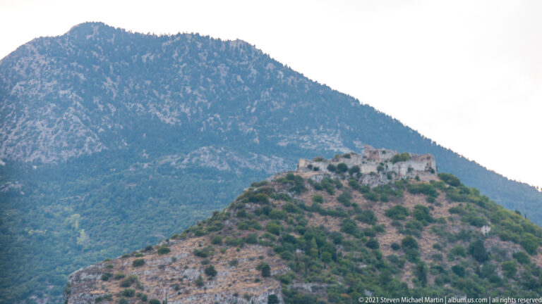Stone fortifications crown a steep ridge at Mystras with a mountain slope rising behind.