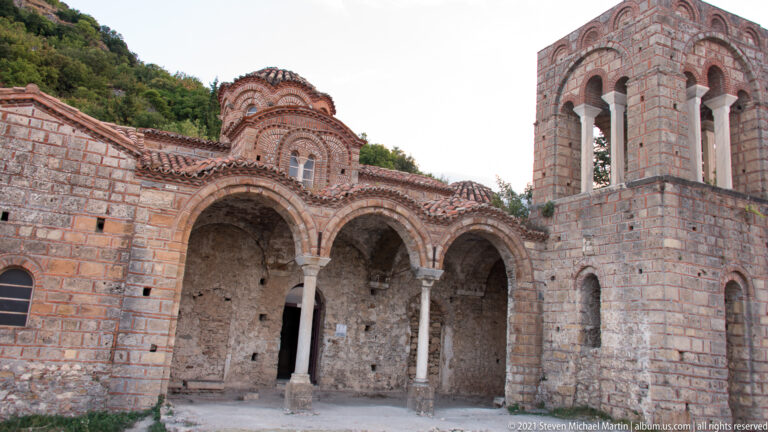 Byzantine church at Mystras with three-arched portico, slender columns, tiled dome, and tall open bell tower.