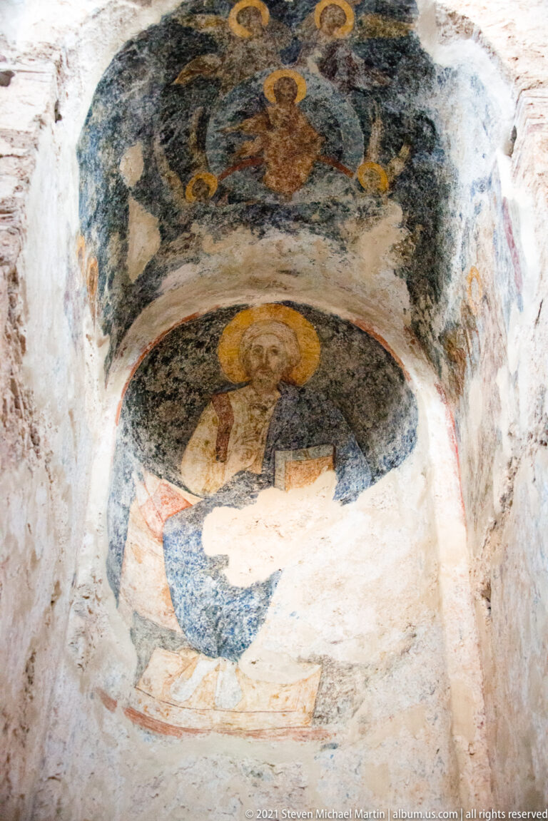 Weathered Byzantine fresco of a haloed sacred figure in a curved niche inside St. Sophia at Mystras.