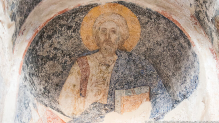 Weathered Byzantine fresco of a haloed Christ holding a book inside St. Sophia at Mystras.