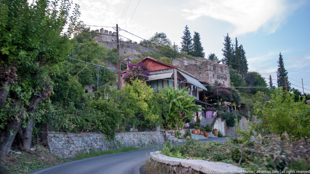 Curving road and hillside houses lie below the stone fortifications of Mystras.