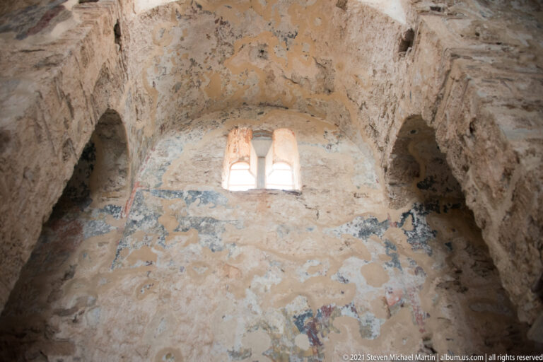 Twin-light arched window high in a worn church wall with traces of faded frescoes and flanking niches.