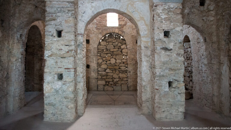 Interior of St. Sophia with masonry piers, arches, small recesses, and a central opening blocked with rough stone.